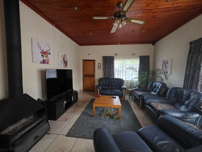 Spacious living room featuring a wood-burning fireplace, timber-clad ceiling with a ceiling fan, and tiled flooring.
