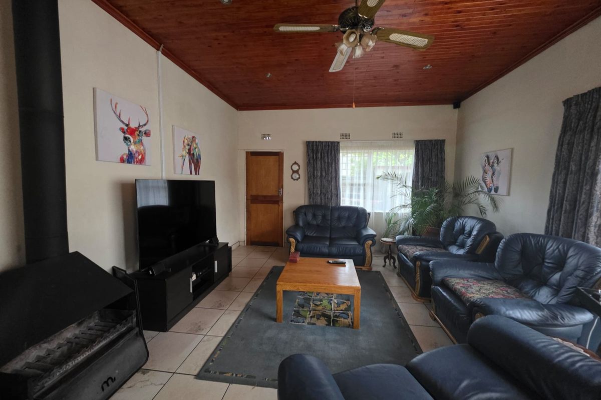 Spacious living room featuring a wood-burning fireplace, timber-clad ceiling with a ceiling fan, and tiled flooring.