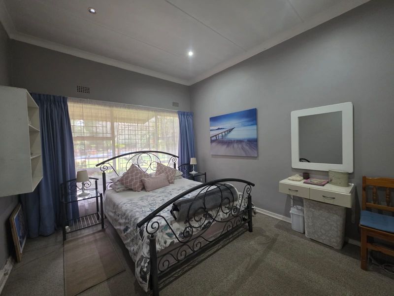 A spacious bedroom featuring neutral grey walls, carpeted flooring, recessed downlighting, and a large window allowing for natural light.