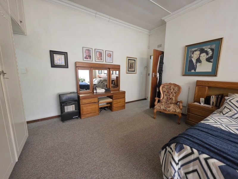 A spacious bedroom featuring neutral walls, carpeted flooring, built-in cupboards, and a gas heater for added warmth.