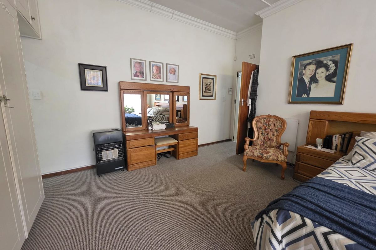 A spacious bedroom featuring neutral walls, carpeted flooring, built-in cupboards, and a gas heater for added warmth.