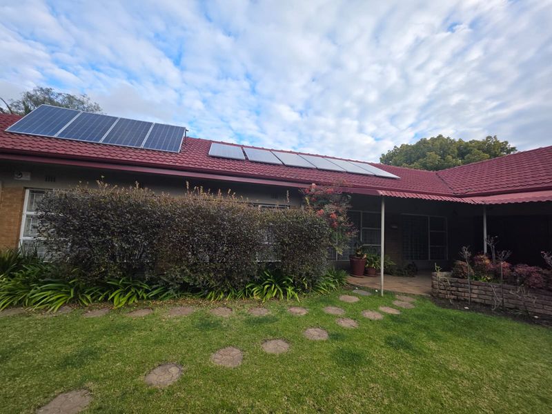 Rear view of the house featuring a tiled roof with installed solar panels, a covered patio area, and a landscaped garden with a stone path.