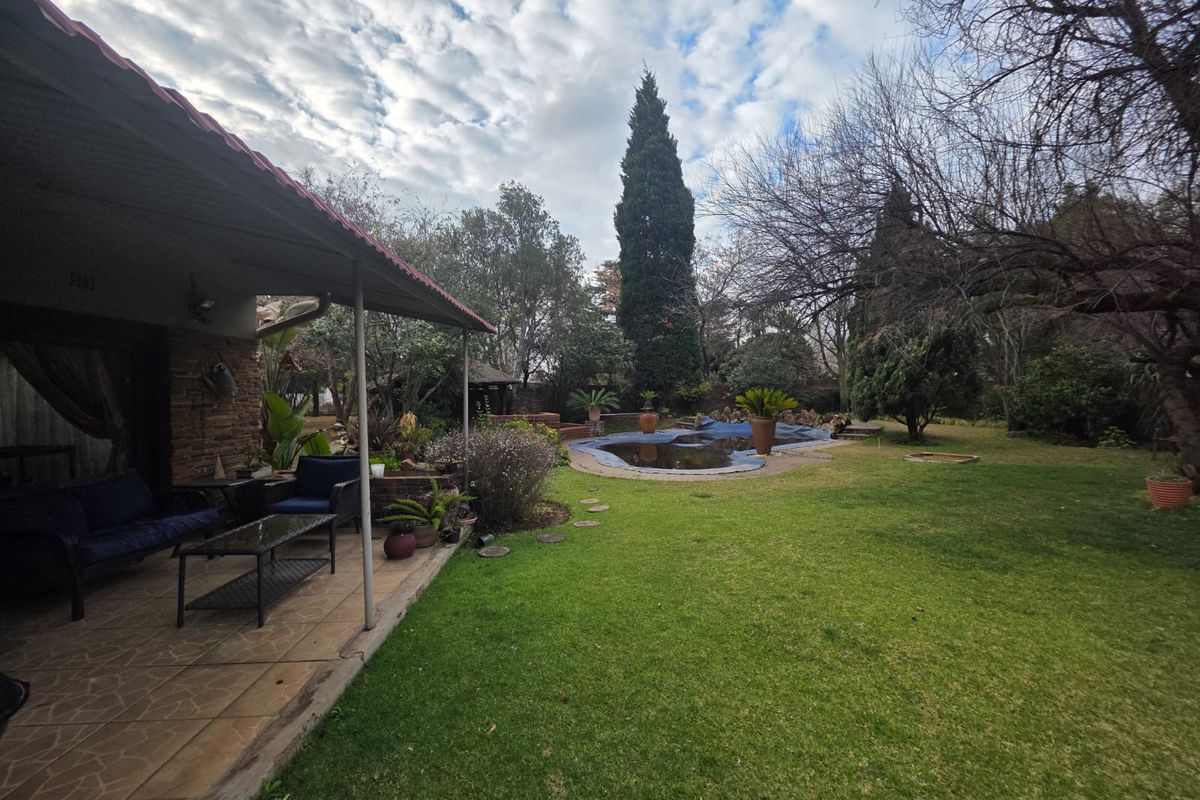Rear garden view featuring a covered patio area, lawn, and a swimming pool with a cover.