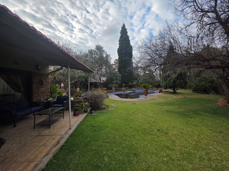 Rear garden view featuring a covered patio area, lawn, and a swimming pool with a cover.