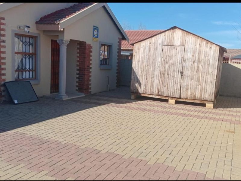 Rear exterior view of the property featuring a paved courtyard area and a detached wooden storage shed.