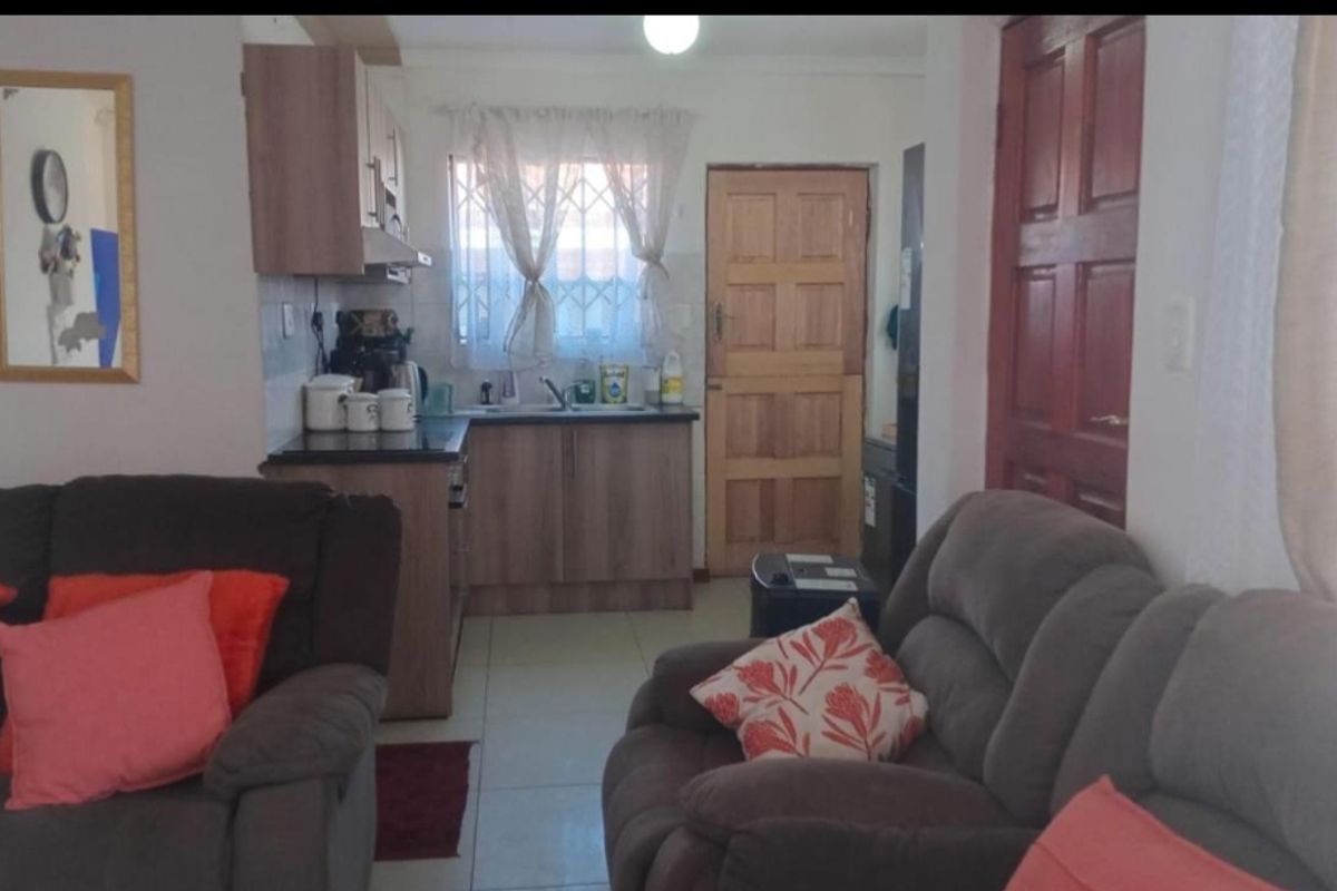 Open plan living area featuring a compact kitchen with built-in cabinetry and tiled flooring, leading to an exterior timber door.