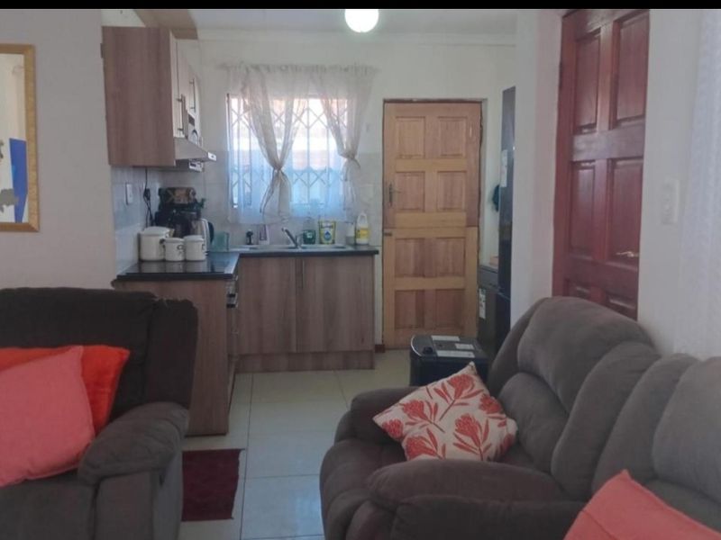 Open plan living area featuring a compact kitchen with built-in cabinetry and tiled flooring, leading to an exterior timber door.