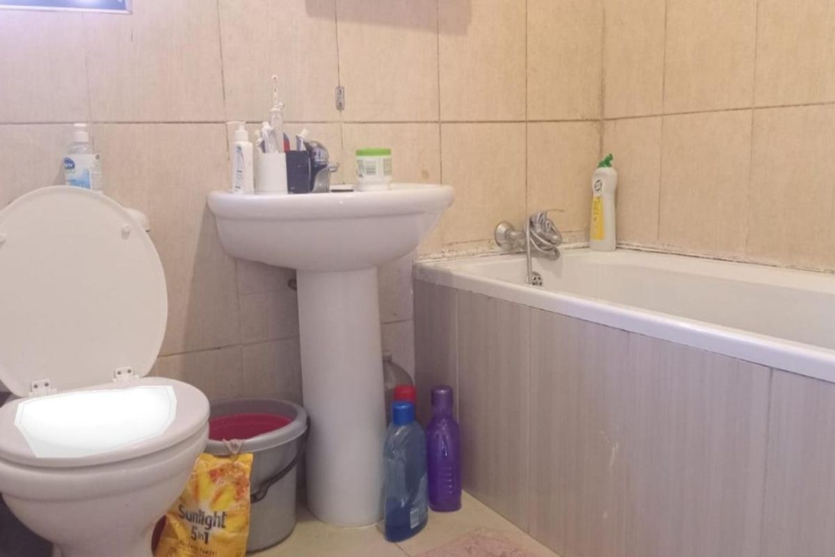 A functional bathroom featuring a pedestal basin, bathtub, and toilet with tiled wall finishes, requiring cosmetic updates to improve its overall condition.