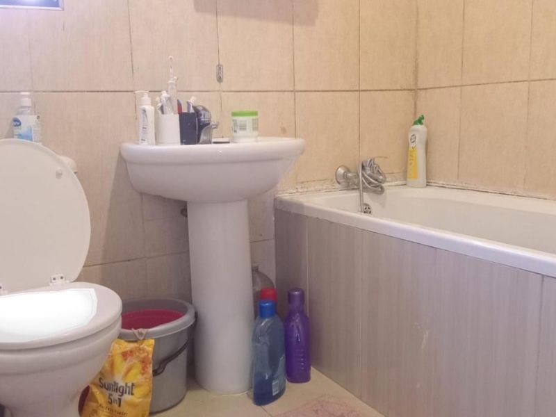 A functional bathroom featuring a pedestal basin, bathtub, and toilet with tiled wall finishes, requiring cosmetic updates to improve its overall condition.