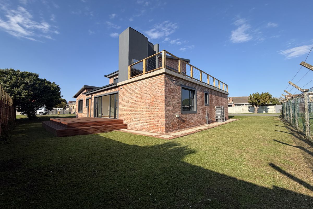 Rear view of a modern house featuring exposed brickwork, a timber deck, and an upper-level balcony with steel cable railings.