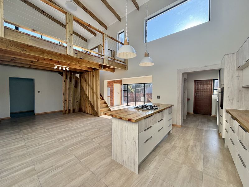 Spacious open-plan living area featuring a modern kitchen island with gas hob, mezzanine level, and high ceilings with exposed timber beams.