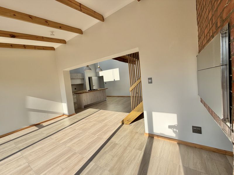 Spacious open-plan living area featuring exposed timber beams, tiled floors, a built-in fireplace, and a seamless transition to the kitchen and staircase.