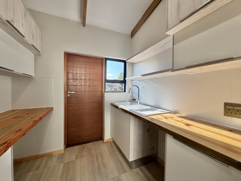 A modern, well-maintained scullery featuring timber countertops, built-in cabinetry, a stainless steel sink, and exposed ceiling beams.