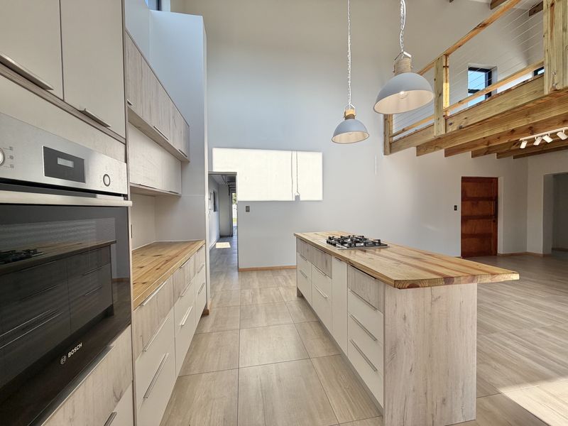 Modern open-plan kitchen featuring light wood-look cabinetry, timber countertops, a central island with a gas hob, and a mezzanine level overlooking the space.