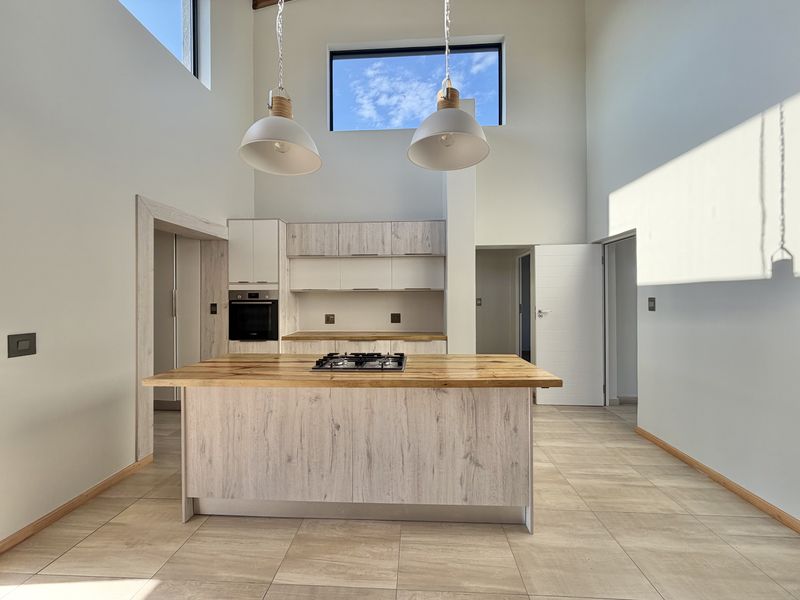 Modern kitchen featuring a central island with a timber countertop, built-in oven, gas hob, and high ceilings with clerestory windows for natural light.