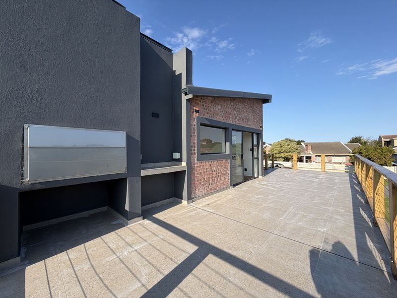Spacious outdoor balcony featuring tiled flooring, a built-in braai, and timber balustrades, offering a clean and functional entertainment area.