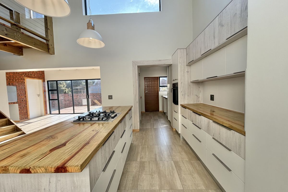 Modern kitchen featuring a central island with gas hob, timber countertops, sleek cabinetry, and high ceilings with a clerestory window for natural light.
