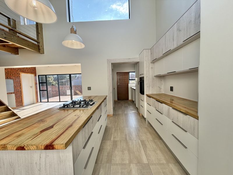 Modern kitchen featuring a central island with gas hob, timber countertops, sleek cabinetry, and high ceilings with a clerestory window for natural light.