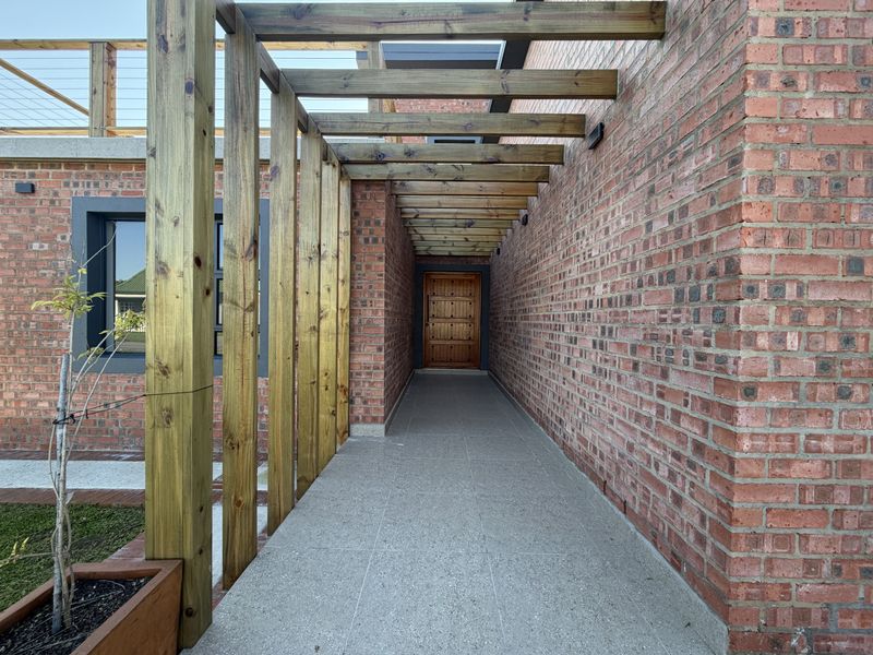 A striking entrance featuring a solid timber front door, protected by a modern timber pergola and finished with high-quality tiled flooring and exposed brickwork.