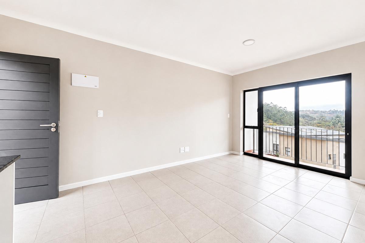 A bright, empty living area featuring neutral tiled flooring, a modern dark-toned door, and large sliding glass doors leading to a balcony with scenic views.