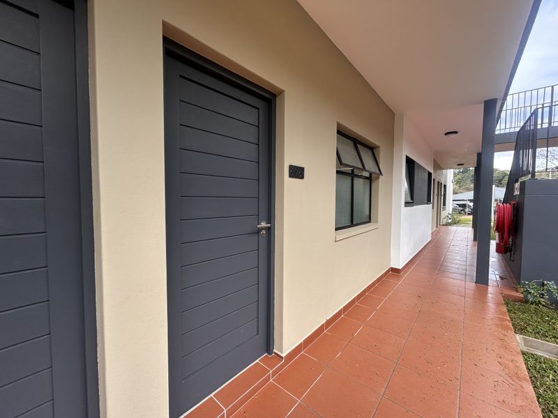 Exterior view of an apartment entrance featuring a tiled walkway, modern dark grey door, and an awning window.