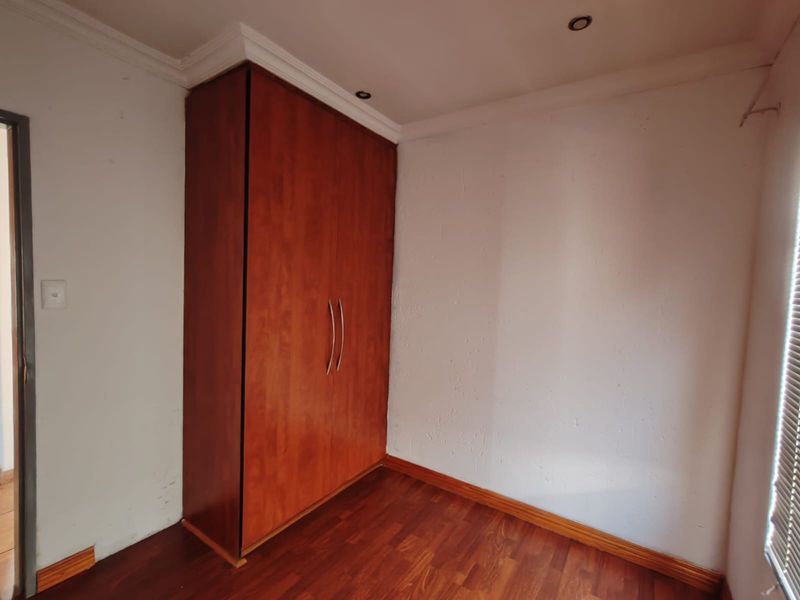 A clean, empty bedroom featuring warm-toned laminate flooring, a built-in wooden wardrobe, and recessed ceiling lighting.