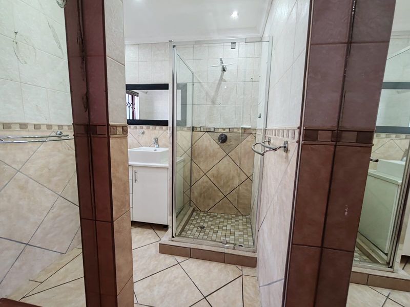 A functional bathroom featuring a glass-enclosed shower, a vanity cabinet with a basin, and neutral-toned wall and floor tiling.
