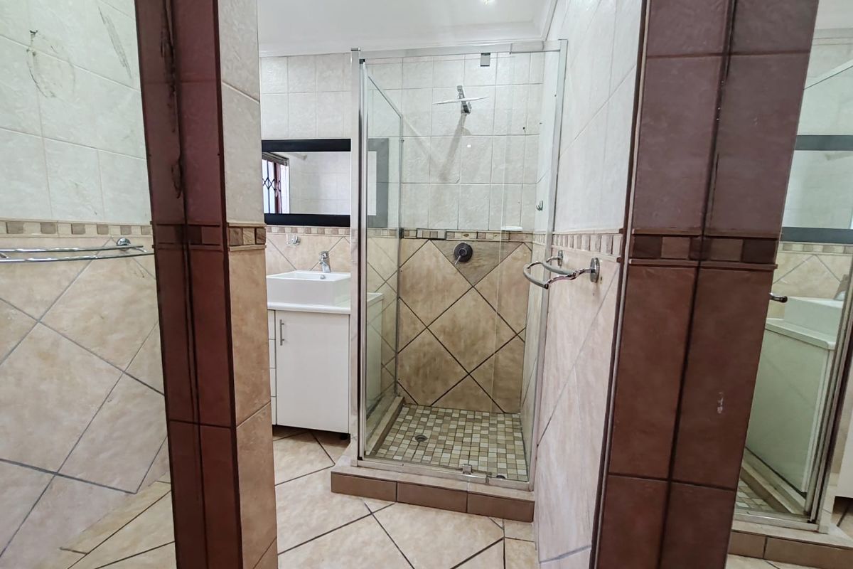 A functional bathroom featuring a glass-enclosed shower, a vanity cabinet with a basin, and neutral-toned wall and floor tiling.
