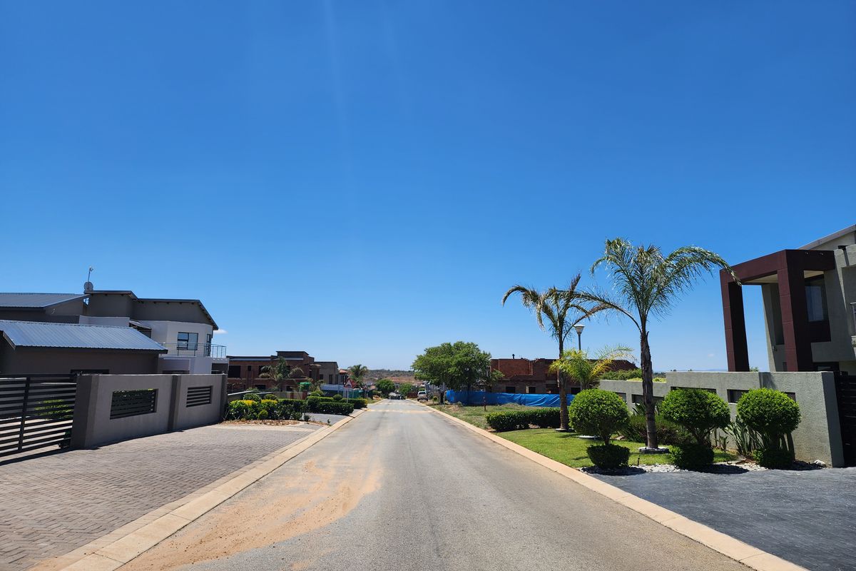A clear street view of a modern residential estate featuring paved driveways, manicured landscaping, and well-maintained boundary walls under a clear blue sky.