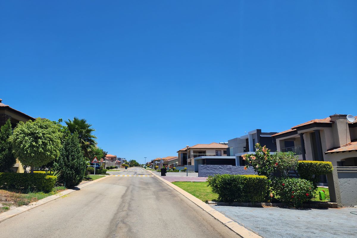 A clear street view of a well-maintained residential estate with paved roads, driveways, and established landscaping.