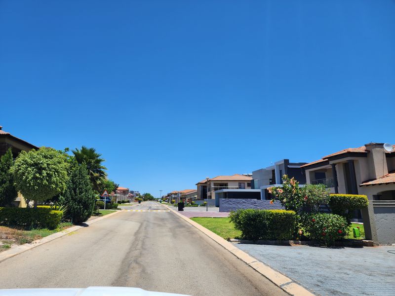 A clear street view of a well-maintained residential estate with paved roads, driveways, and established landscaping.