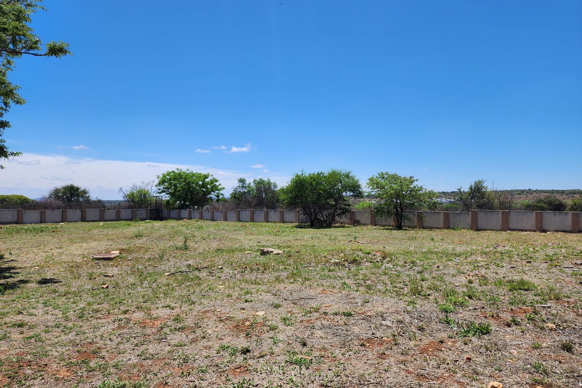 A view of a vacant residential plot featuring a perimeter wall and natural vegetation under a clear blue sky.