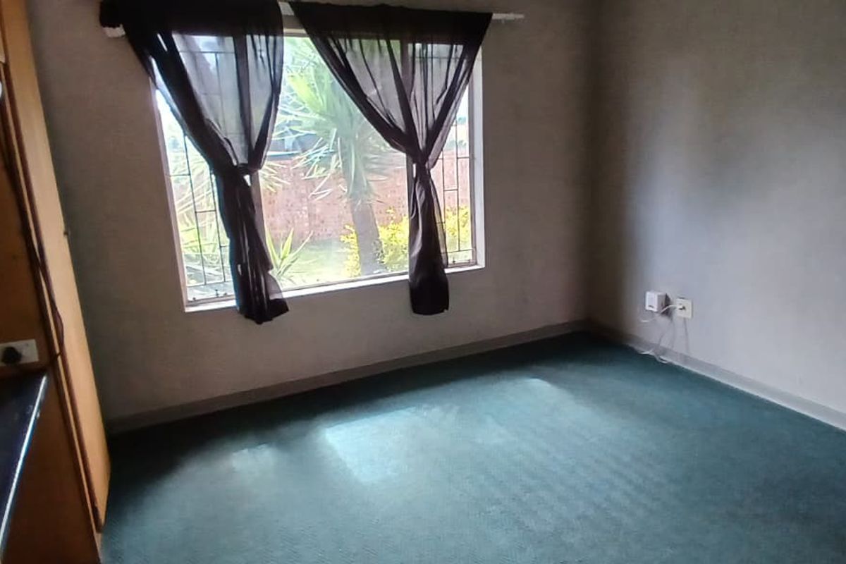 An empty bedroom featuring built-in cabinetry, carpeted flooring, and a window with security bars, offering a blank canvas for renovation.