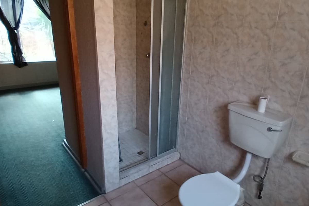 A functional bathroom featuring a shower enclosure and toilet with dated ceramic wall and floor tiling.