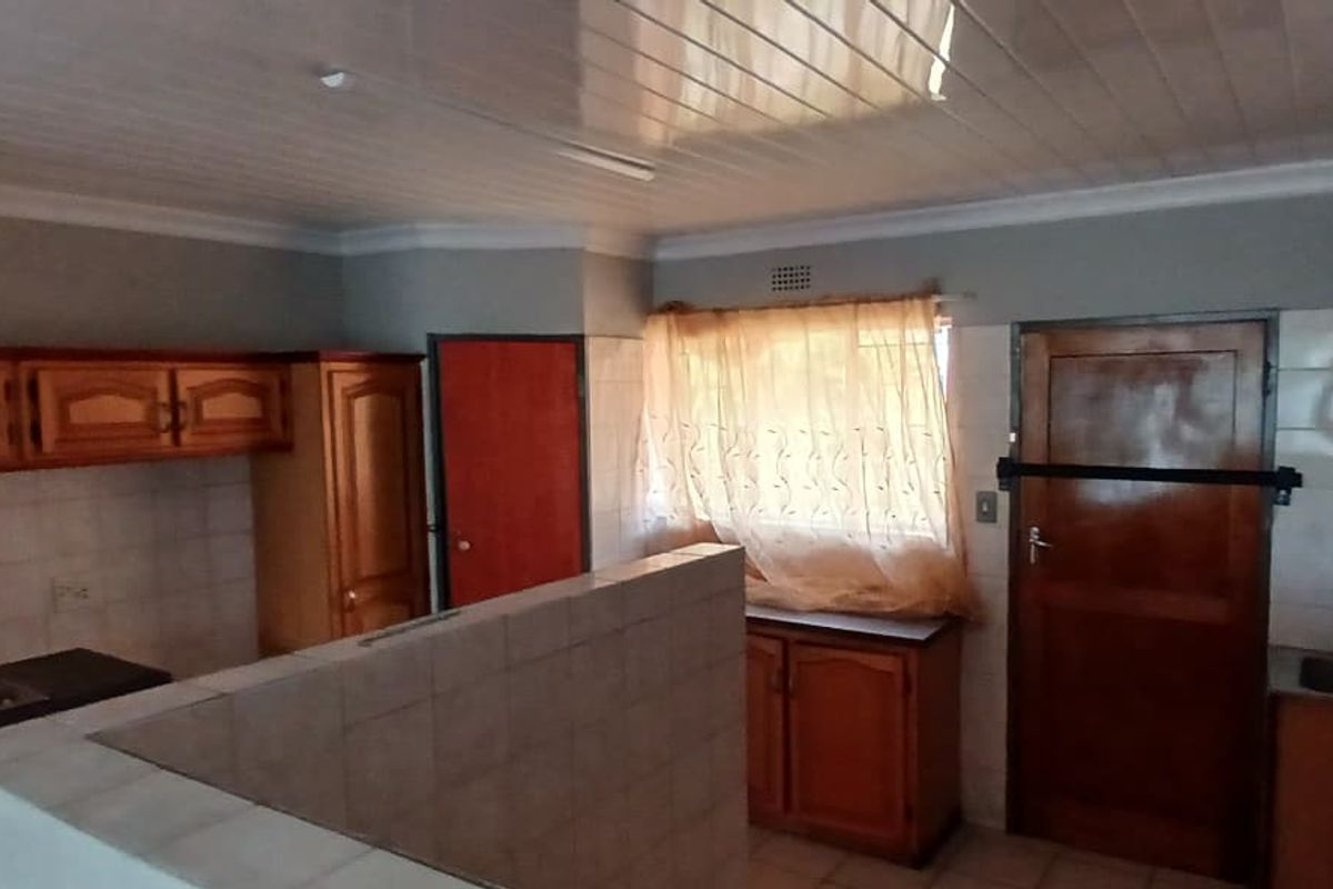 A dated kitchen featuring wooden cabinetry, tiled splashbacks, a built-in stove, and a sink, with a PVC ceiling and tiled flooring.