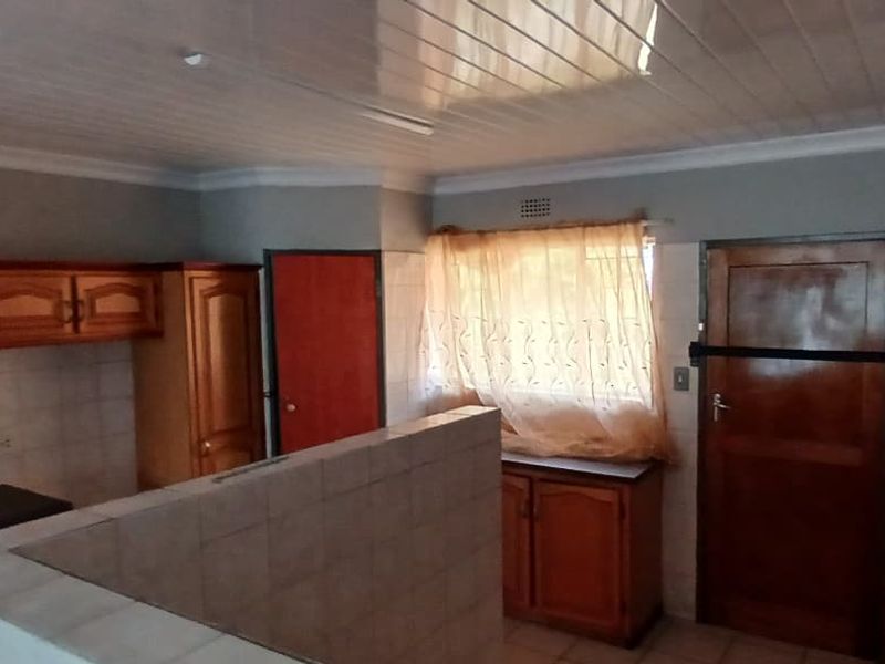 A dated kitchen featuring wooden cabinetry, tiled splashbacks, a built-in stove, and a sink, with a PVC ceiling and tiled flooring.