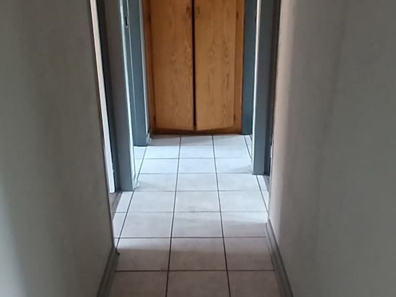 A functional hallway featuring tiled flooring and a built-in wooden cupboard, providing access to adjacent rooms.