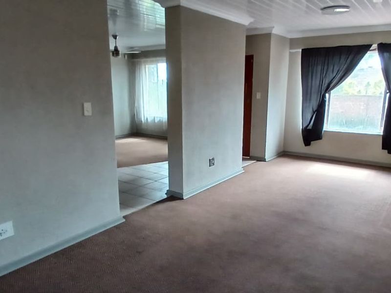Spacious, empty living area featuring neutral wall tones, carpeted flooring, and a secondary tiled space visible through the central partition.
