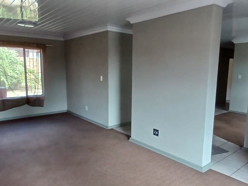 Spacious, empty living area featuring carpeted floors, glossy ceiling panels, and large windows with security bars, offering a neutral canvas for interior design.