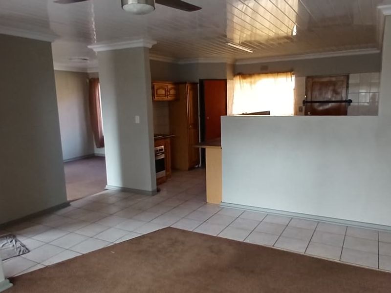 An open-plan living and kitchen area featuring a mix of tiled and carpeted flooring, a ceiling fan, and functional built-in kitchen cabinetry.