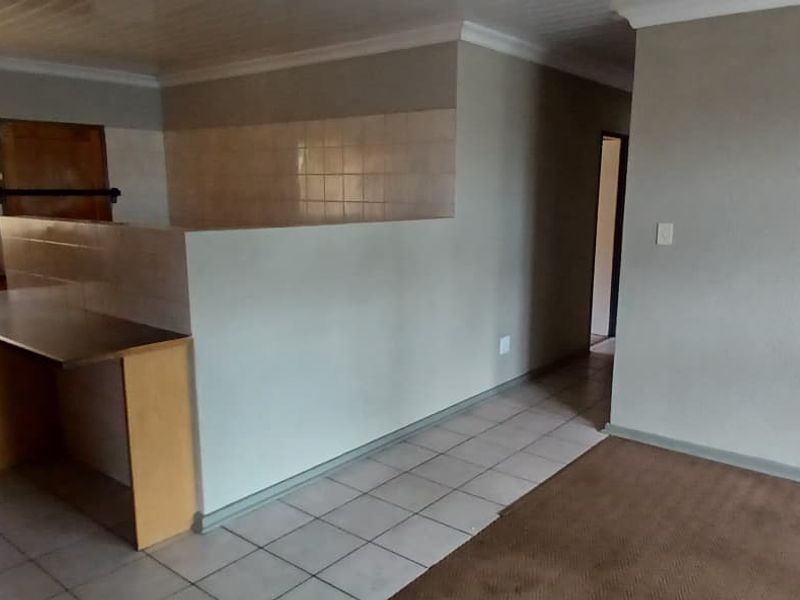 An open-plan living and kitchen area featuring tiled flooring, built-in cabinetry, and a breakfast bar, offering a functional layout ready for modernization.