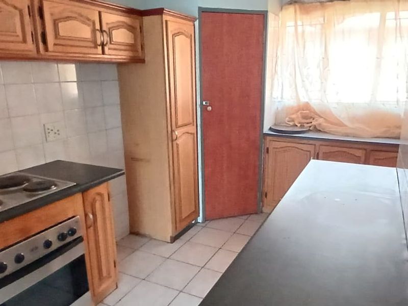 A dated kitchen featuring wooden cabinetry, an electric hob, built-in oven, tiled backsplash, and a breakfast bar counter.