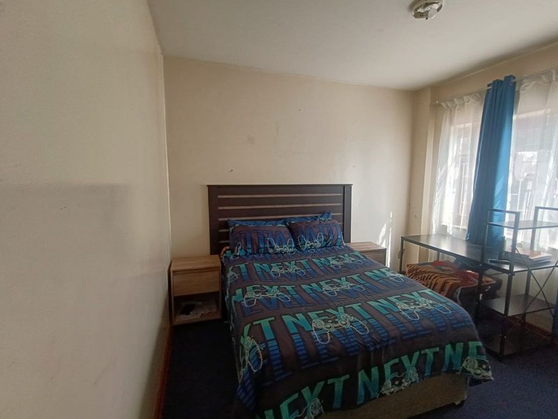 A standard bedroom featuring dark carpeting and a window with fitted curtain rails, requiring minor cosmetic updates to the wall finishes.