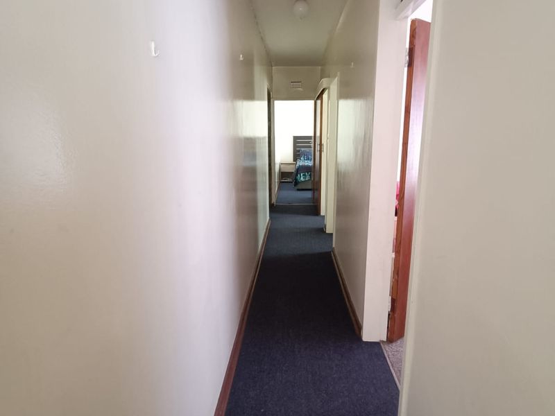 A narrow residential hallway featuring dark carpet flooring and plain walls, providing access to adjacent rooms within the flat.