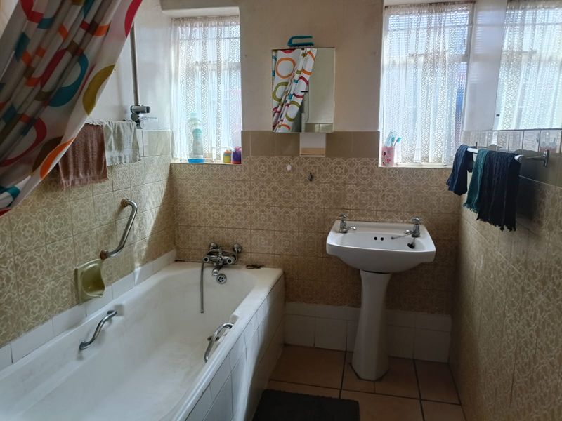 A functional bathroom featuring a bathtub with a grab rail, a pedestal basin, and dated wall tiling throughout.