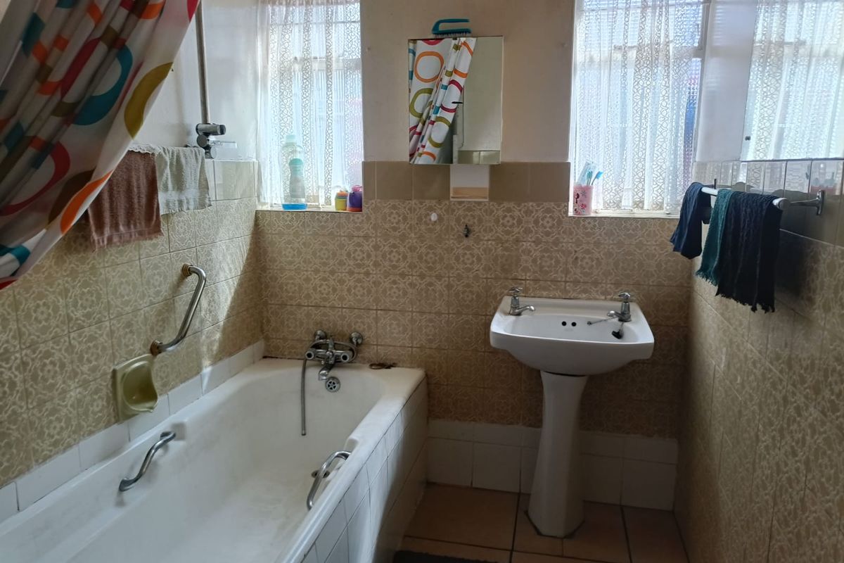 A functional bathroom featuring a bathtub with a grab rail, a pedestal basin, and dated wall tiling throughout.