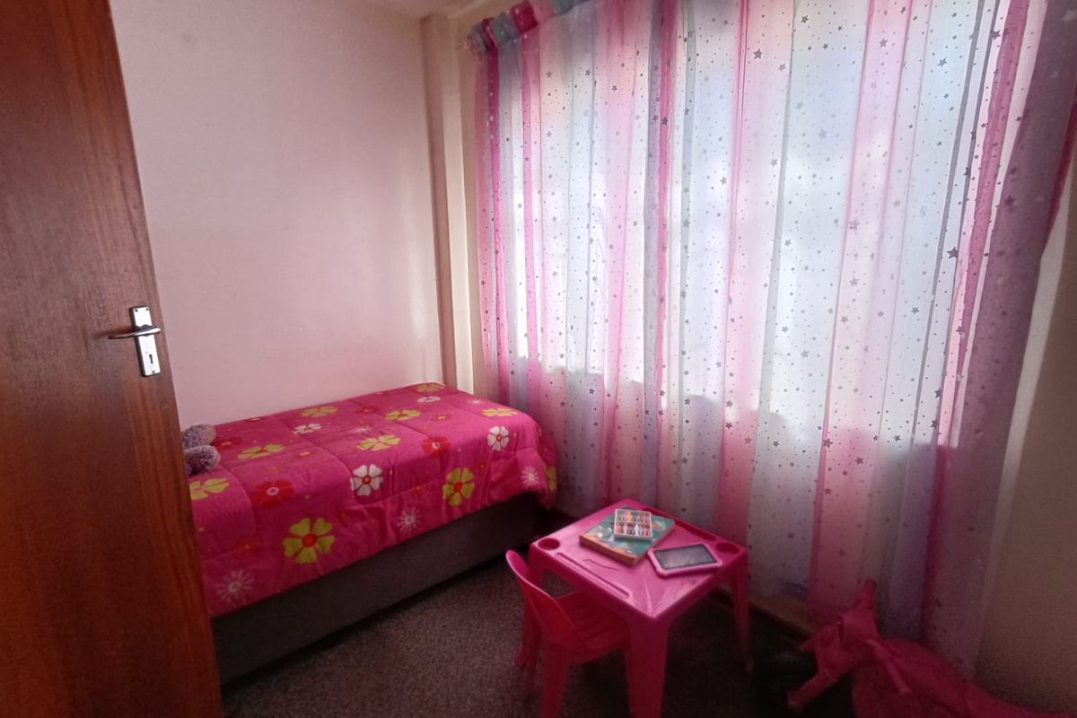 A compact bedroom featuring carpeted flooring and a wooden door, currently utilized as a child's room.