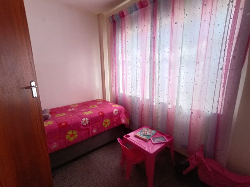 A compact bedroom featuring carpeted flooring and a wooden door, currently utilized as a child's room.