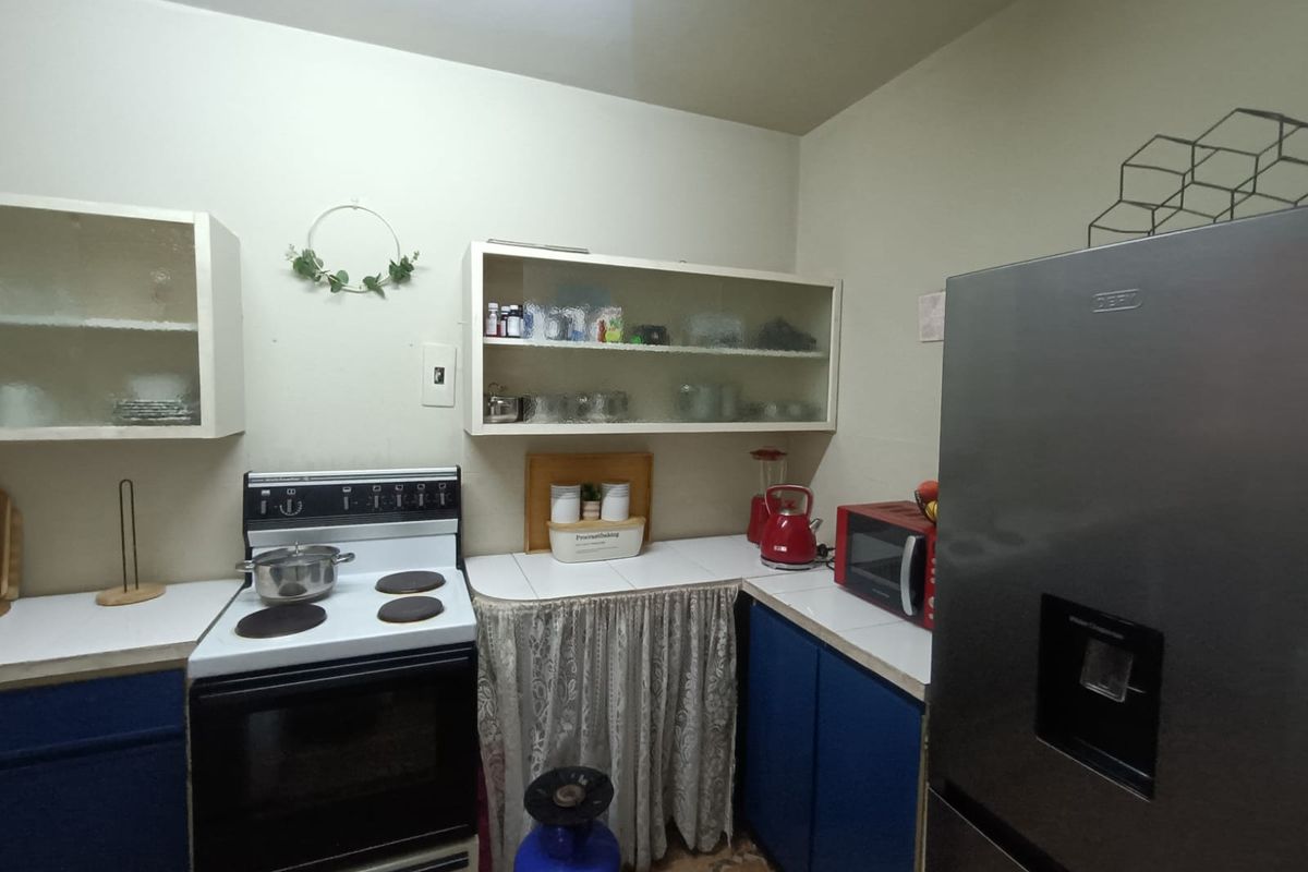 A functional kitchen featuring tiled countertops, blue base cabinetry, and wall-mounted glass-fronted storage units, providing a practical layout for daily meal preparation.