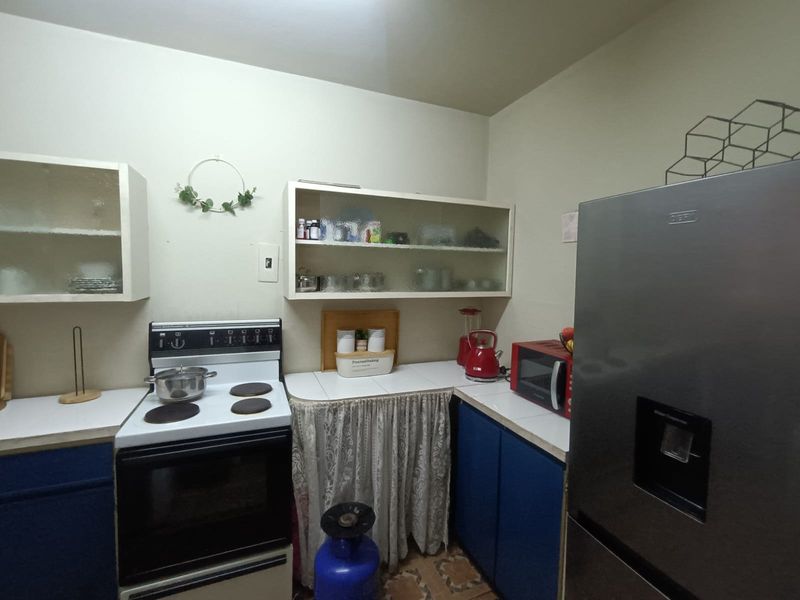 A functional kitchen featuring tiled countertops, blue base cabinetry, and wall-mounted glass-fronted storage units, providing a practical layout for daily meal preparation.